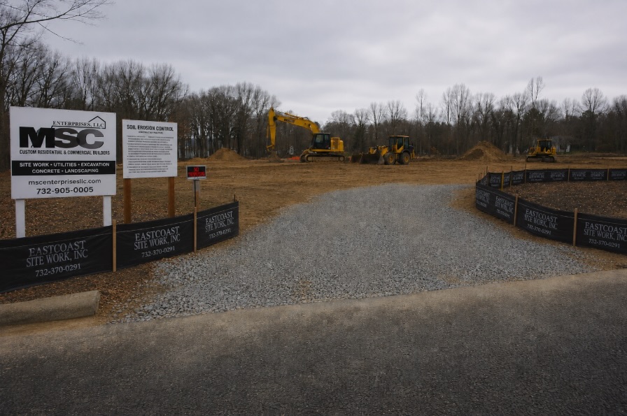 Silt fence installed along the perimeter of an active New Jersey construction site with a stabilized entrance tracking pad in the foreground
